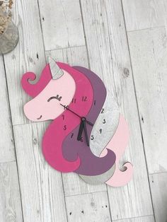 a wooden clock with a pink and purple unicorn face on it's face is sitting on the floor