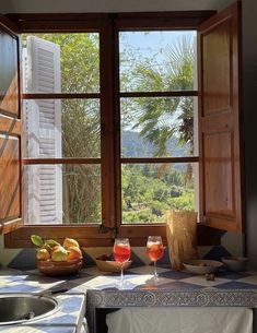 two glasses of wine sit on a counter in front of a window with an outside view