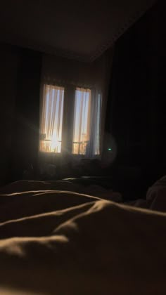 the sun shines through two windows in a dark room with bed linens on it