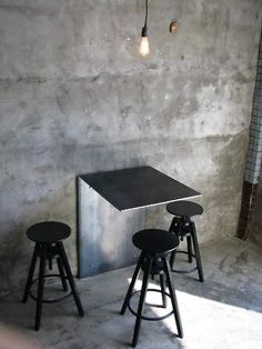 three stools and a table in front of a concrete wall with a light bulb hanging over it