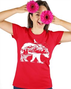 a woman holding two pink flowers in front of her face while wearing a red shirt