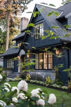 a blue house with lots of windows and bushes in the front yard, along with white flowers