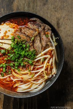 a bowl filled with noodles and meat on top of a wooden table