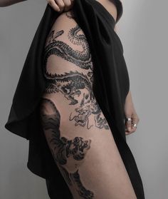 a woman with dragon tattoos on her leg and thigh, holding onto a black dress