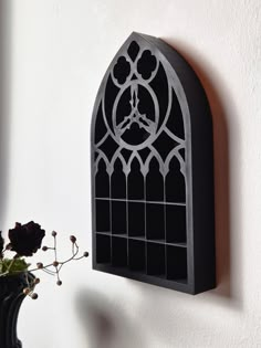 a black stained glass window mounted to the side of a wall next to a vase with flowers