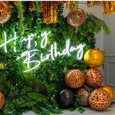 a happy birthday sign surrounded by jungle plants and balloons in front of a green wall