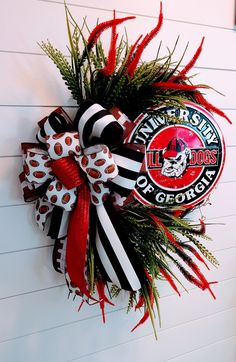 University of Georgia Bulldogs Wreath  This wreath was inspired by Football Season It's made of UV resistant Foilage and complimented by beautiful, high quality wired Ribbons. The multi Ribbon Bow measures 13.5 wide and 20-22 inches long. The Georgia Bulldogs Tin sign measuring 11.5  inches round, is removable. The overall wreath measures 22-24 across and 24-26 long. This turned out so cute and it's ready for it's new home Go Dawgs Georgia Bulldog Wreath, Multi Ribbon Bow, Football Decor, Go Dawgs, Georgia Football, Football Decorations, University Of Georgia, Georgia Bulldogs, Wired Ribbon