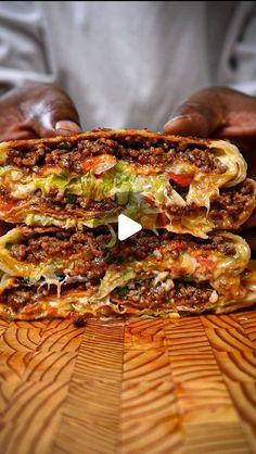 a person holding a stack of food on top of a wooden table