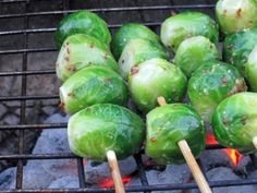 several green peppers cooking on a grill with wooden skewers sticking out of them