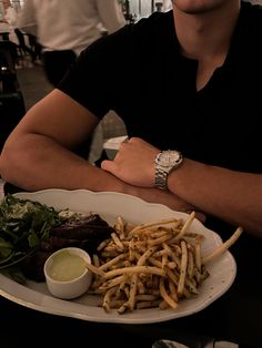 a man sitting at a table with a plate of food in front of him that has fries and greens on it