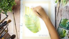 a person is painting a green leaf with watercolors