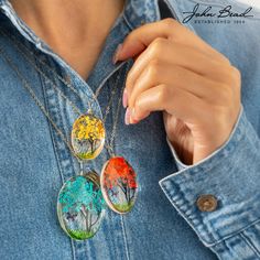 the woman is wearing three necklaces with different designs on them, including trees and leaves