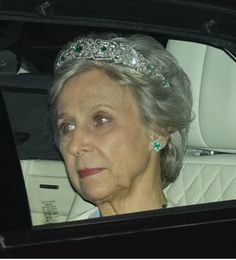 an older woman wearing a tiara and sitting in the back seat of a car