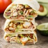 three burritos stacked on top of each other with avocado and tomatoes in the background