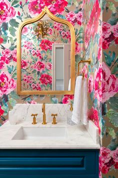 a bathroom with floral wallpaper, gold framed mirror and blue vanity sink in front of it