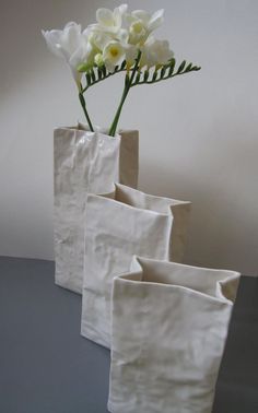 three white vases with flowers in them sitting on a gray countertop next to each other