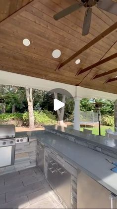 an outdoor kitchen with stainless steel grills and ceiling fans on the outside patio area