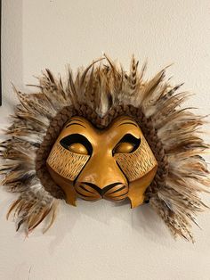 a lion mask mounted to the wall with feathers on it's head and eyes