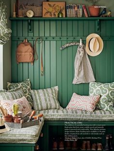 a green bench with many pillows and hats on it's headrests in front of a green wall