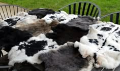 several black and white sheepskin rugs sitting on top of a wooden chair in the grass