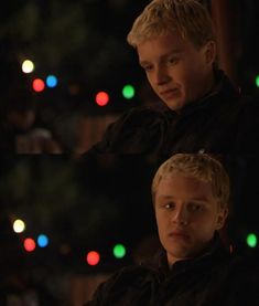 two young men standing next to each other in front of a christmas tree with lights