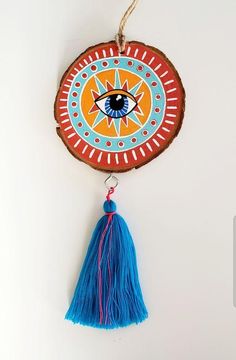 a wooden slice with a blue tassel hanging from it's side and an eye painted on the front