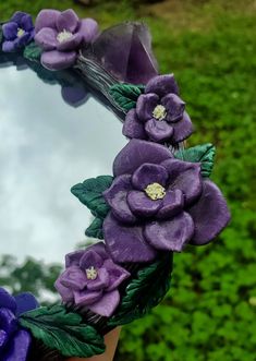 a mirror with purple flowers on it in front of some green grass and bushes,