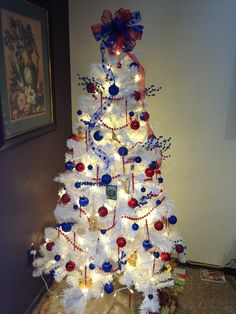 a white christmas tree decorated with red, white and blue ornaments is on the floor