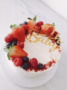 a white cake with strawberries and blueberries on top is decorated with gold lettering