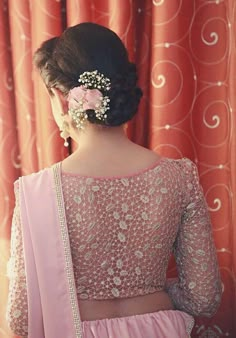 a woman wearing a pink sari and flower in her hair, looking out the window