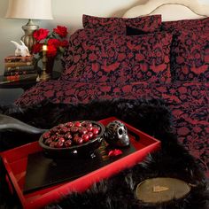 a bed with red and black comforters, pillows and a tray filled with cherries