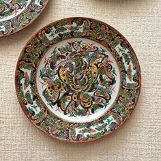 two plates with designs on them sitting next to each other in front of a table cloth