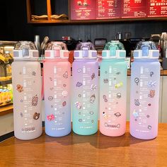 four different colored water bottles sitting on top of a wooden table in front of a counter