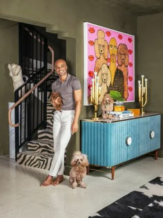 a man standing next to a dog in front of a stair case with paintings on the wall