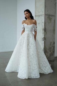 a woman in a white wedding dress standing against a wall