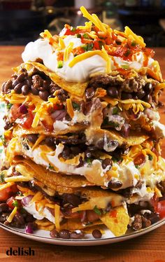 a stack of nachos on a plate topped with sour cream and black beans