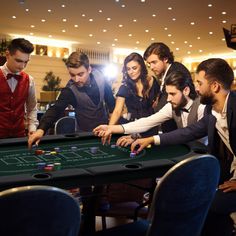 a group of people standing around a black table playing roulejack in a casino