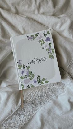 an open book with flowers on it sitting on a white sheet covered bed next to a pillow