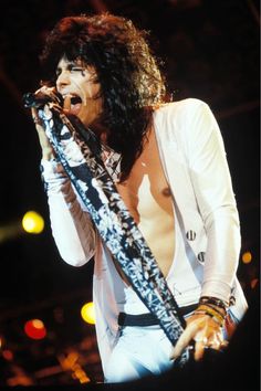 a man with long hair and no shirt on holding a microphone in his hand while singing