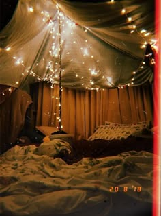 a bed covered in white sheets under a tent with lights on the ceiling and curtains