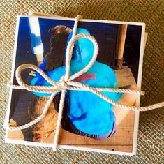 a blue stuffed animal wrapped in twine on top of a piece of cardboard with rope