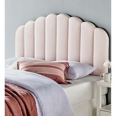 a pink headboard on top of a white bed with pillows and throw pillows in front of it