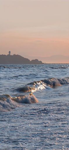 the waves are rolling in to shore at sunset or dawn, with an island in the distance