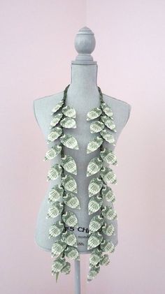 a white mannequin with green leaves on it's neck and two necklaces hanging from the back