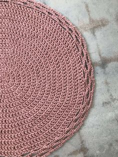 a pink crocheted rug sitting on top of a cement floor