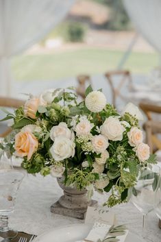 a vase filled with white and peach flowers on top of a table covered in greenery