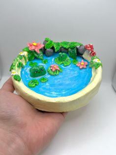 a hand is holding a small cake decorated like a pond