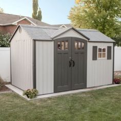 a small shed with two doors and windows in the yard next to a white fence