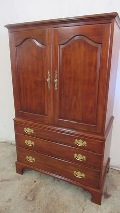 a wooden armoire with two doors and gold handles on the bottom drawer, against a white wall