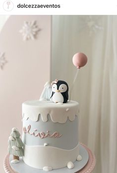 a birthday cake with a penguin on top and an air balloon in the sky above it